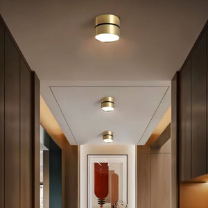 Gold cylindrical flush mount ceiling lights installed in a modern hallway with white ceiling and wood-paneled walls.