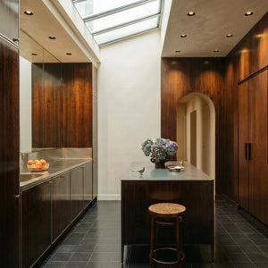 Recessed downlights illuminate a modern kitchen with dark wood cabinetry, stainless steel countertops, and a skylight.