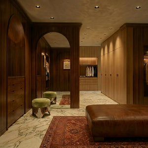 Recessed downlights illuminate a luxurious wooden walk-in closet with marble flooring and built-in cabinetry.