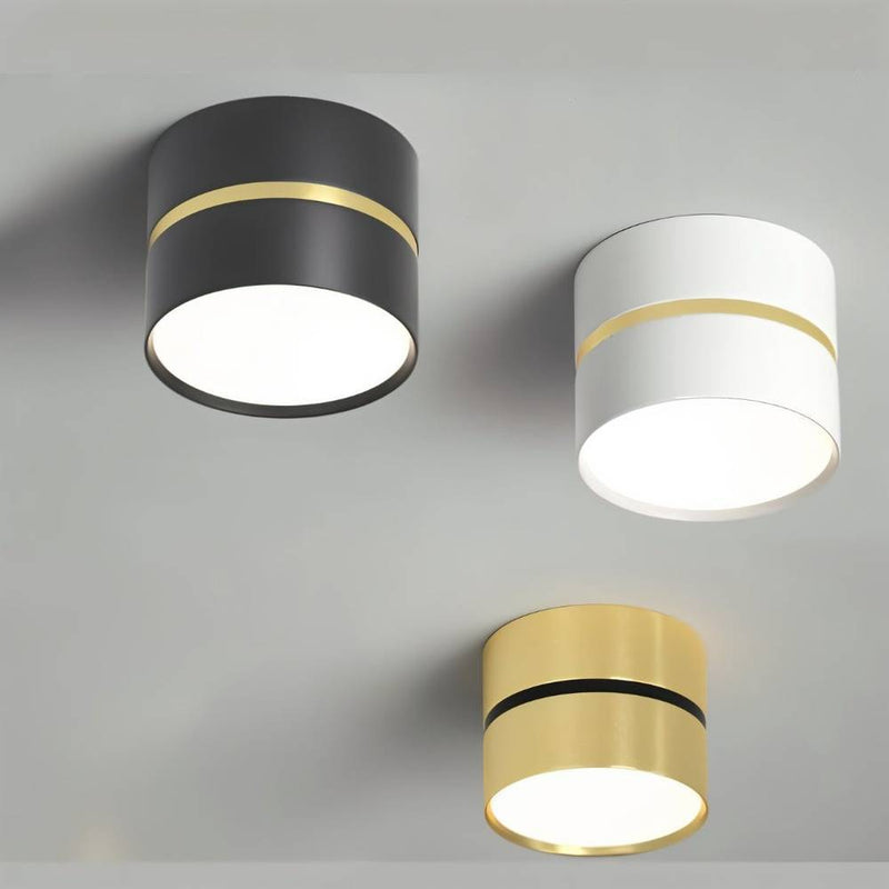 Three cylindrical ceiling downlights in black, white, and brass finishes with gold accent bands on a gray background.