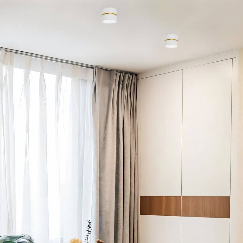 White and brass recessed downlight mounted on a neutral ceiling above a modern bedroom with floor-to-ceiling wardrobe.
