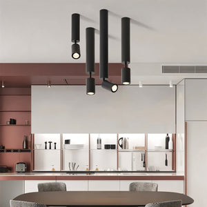 Black cylindrical pendant downlights with warm glowing bulbs suspended above a modern kitchen with terracotta and white cabinetry.