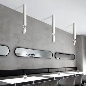 White cylindrical pendant downlight suspended from ceiling above modern salon vanity with mirrors.