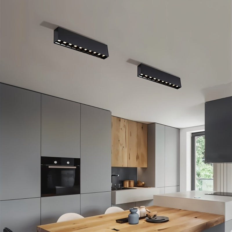 Black linear ceiling downlights installed above a modern kitchen with gray cabinets and wooden dining table.