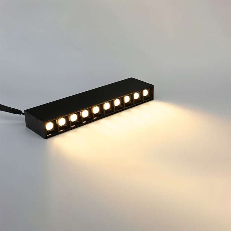Black linear LED downlight with warm white illumination casting light on a neutral surface.