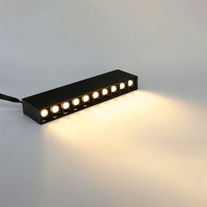 Black linear LED downlight with warm white illumination casting light on a neutral surface.