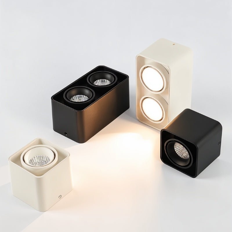 Four cube-shaped LED downlights in cream, black, and bronze finishes displayed on a white background.