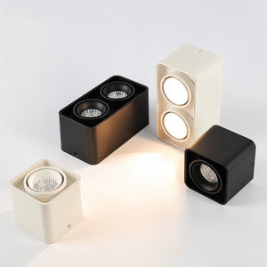 Four cube-shaped LED downlights in cream, black, and bronze finishes displayed on a white background.