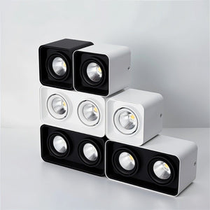 Modular LED downlights in black and white finishes stacked in a pyramid arrangement on a neutral background.