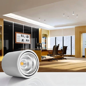 White cylindrical LED downlight with warm gold center displayed in modern office setting with wooden accents.