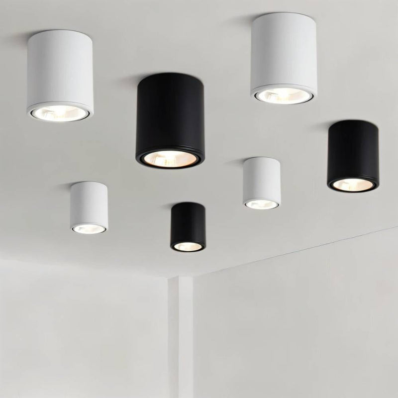 Seven cylindrical ceiling downlights in white and black finishes mounted on a light gray ceiling.