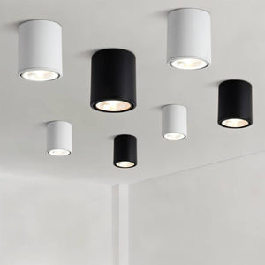 Seven cylindrical ceiling downlights in white and black finishes mounted on a light gray ceiling.