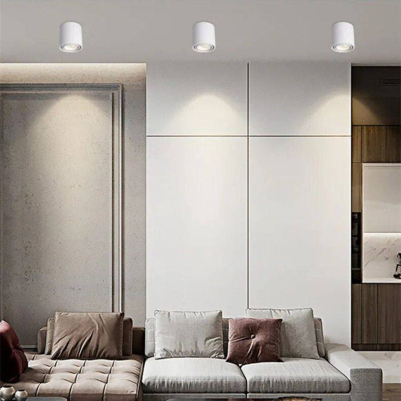 White cylindrical LED downlights mounted on ceiling above modern living room with neutral furnishings.