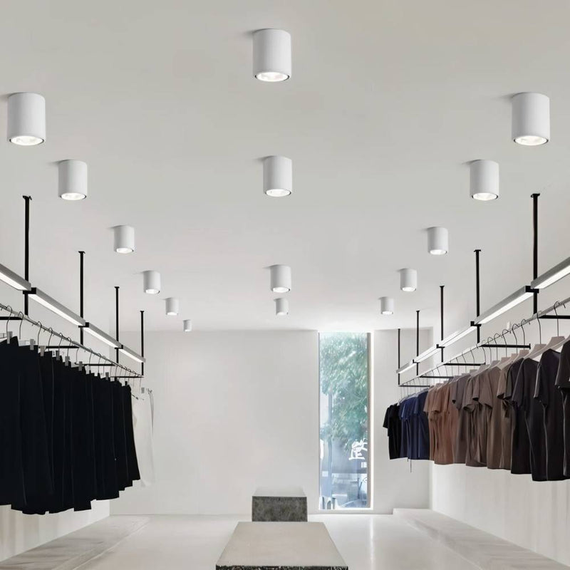 White cylindrical downlight fixtures illuminating a modern retail clothing store with hanging garments.