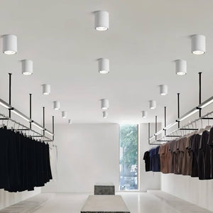 White cylindrical downlight fixtures illuminating a modern retail clothing store with hanging garments.