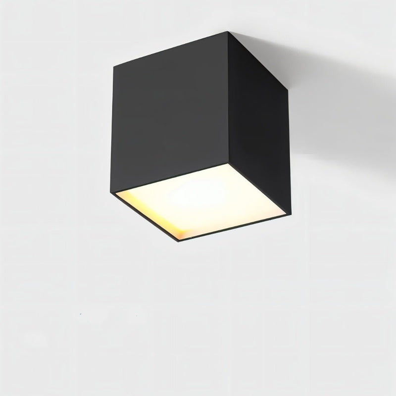 Black cube ceiling downlight with warm white glow on neutral background.