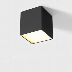 Black cube ceiling downlight with warm white glow on neutral background.