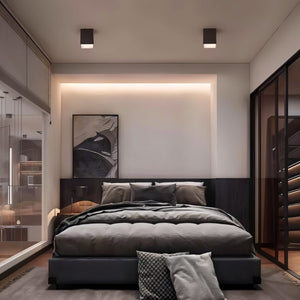 Black recessed downlight fixtures mounted on white ceiling above modern bedroom with dark bed.