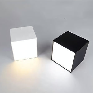 Two cube-shaped downlights with white and black finishes casting warm light on a gray surface.