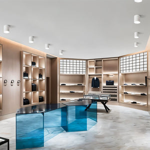 White cylindrical recessed downlights installed in ceiling of modern retail clothing store with wooden shelving and blue display table.