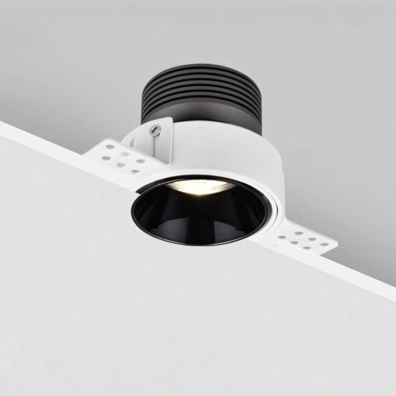 White recessed downlight with black interior trim mounted in ceiling, emitting warm light.