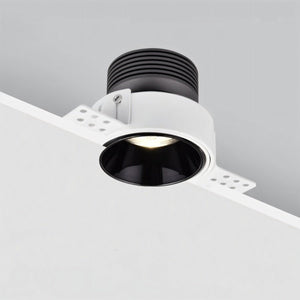 White recessed downlight with black interior trim mounted in ceiling, emitting warm light.