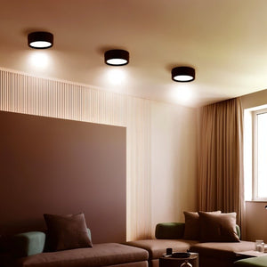 Black round ceiling downlight with warm white glow installed above modern living room seating.