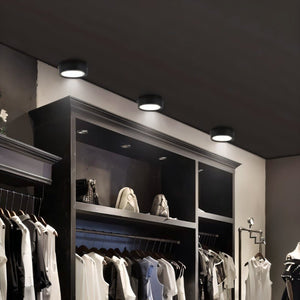 Black ceiling downlight with white LED trim illuminating a retail clothing display with hanging garments.