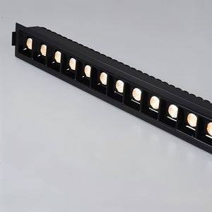 Black linear downlight fixture with multiple recessed warm LED spotlights mounted on white wall.