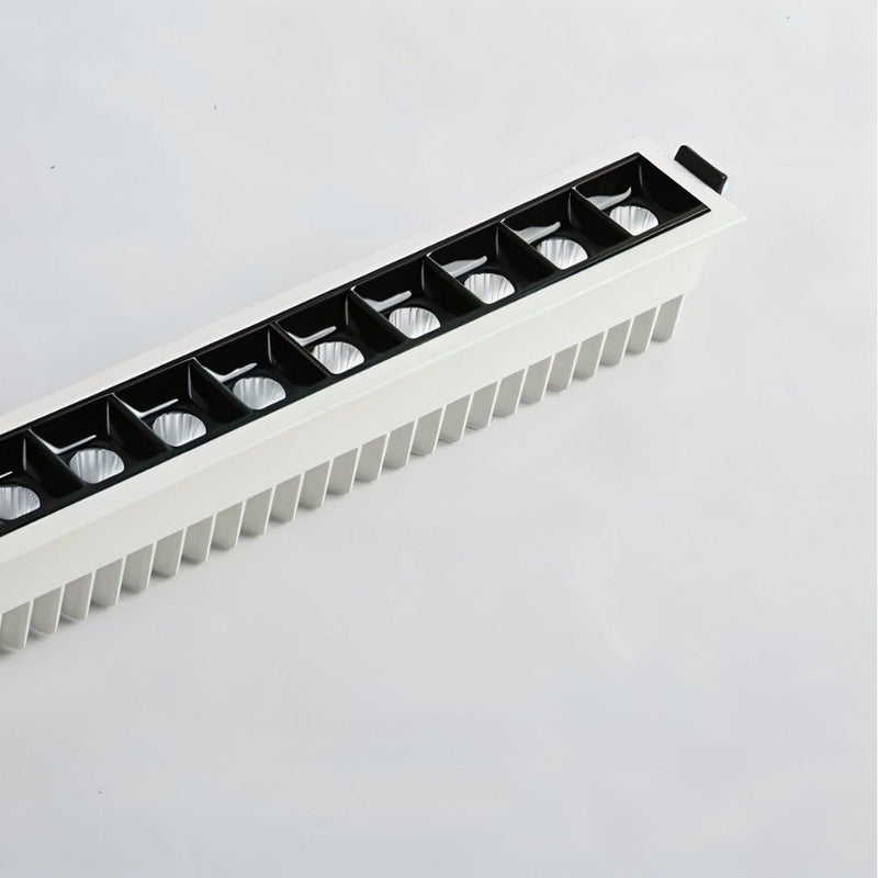Linear recessed downlight with black trim and white ribbed baffle in ceiling against neutral background.