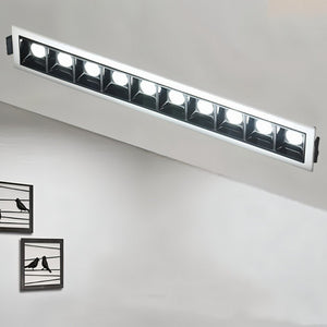 Linear recessed downlight with white trim and black reflectors displaying eight illuminated LED modules against a white ceiling.