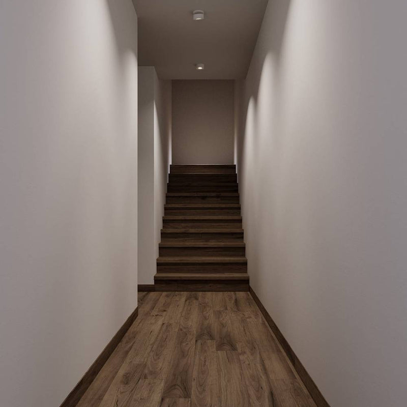 Recessed ceiling light fixture installed in a narrow hallway with white walls and wooden stairs.