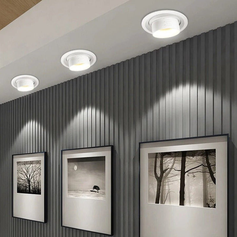 Recessed downlight with white finish mounted on gray corrugated wall with framed black and white photographs.