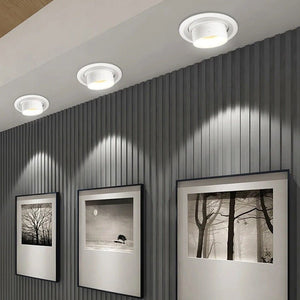 Recessed downlight with white finish mounted on gray corrugated wall with framed black and white photographs.
